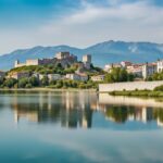 Vista panorámica de Shkoder, Albania, con el histórico Castillo de Rozafa en primer plano y el Lago Skadar al fondo, bajo un cielo azul claro.