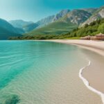 Vista escénica de una playa de arena con agua turquesa cristalina, rodeada de montañas verdes y un cielo azul brillante en vacaciones en Albania.